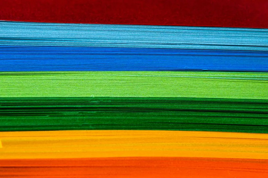 A stack of colored paper sheets in a range of hues, viewed edge-on.